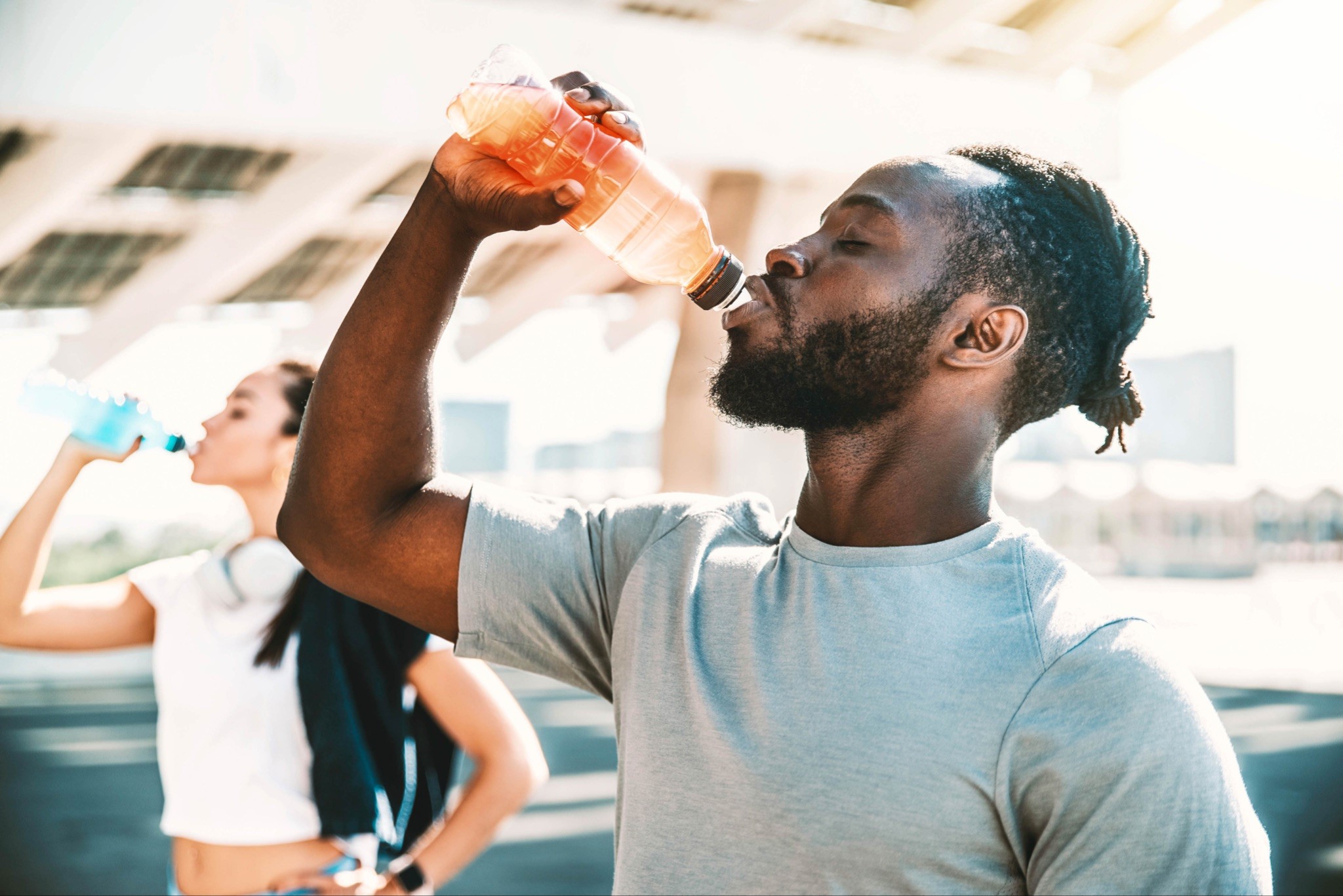 A man and a woman standing next to each other drinking a bottled sports drink after a workout.