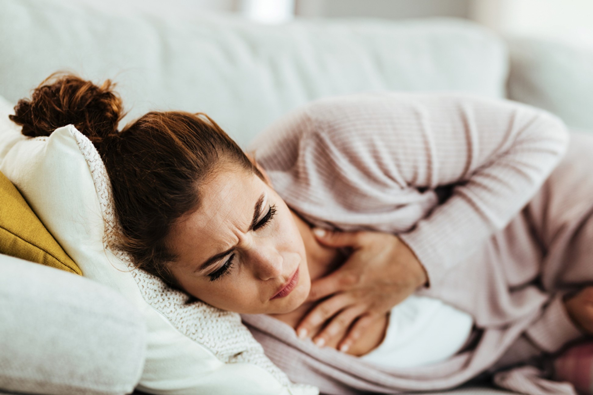 A woman gripping her chest in pain as she lays on the sofa.