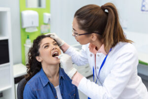 A female doctor examines a female patient’s throat using a tongue depressor in a doctor’s office.