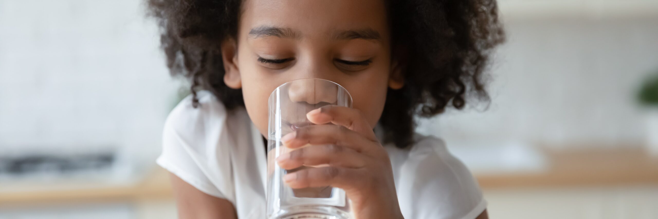 A young girl is drinking a glass of water.