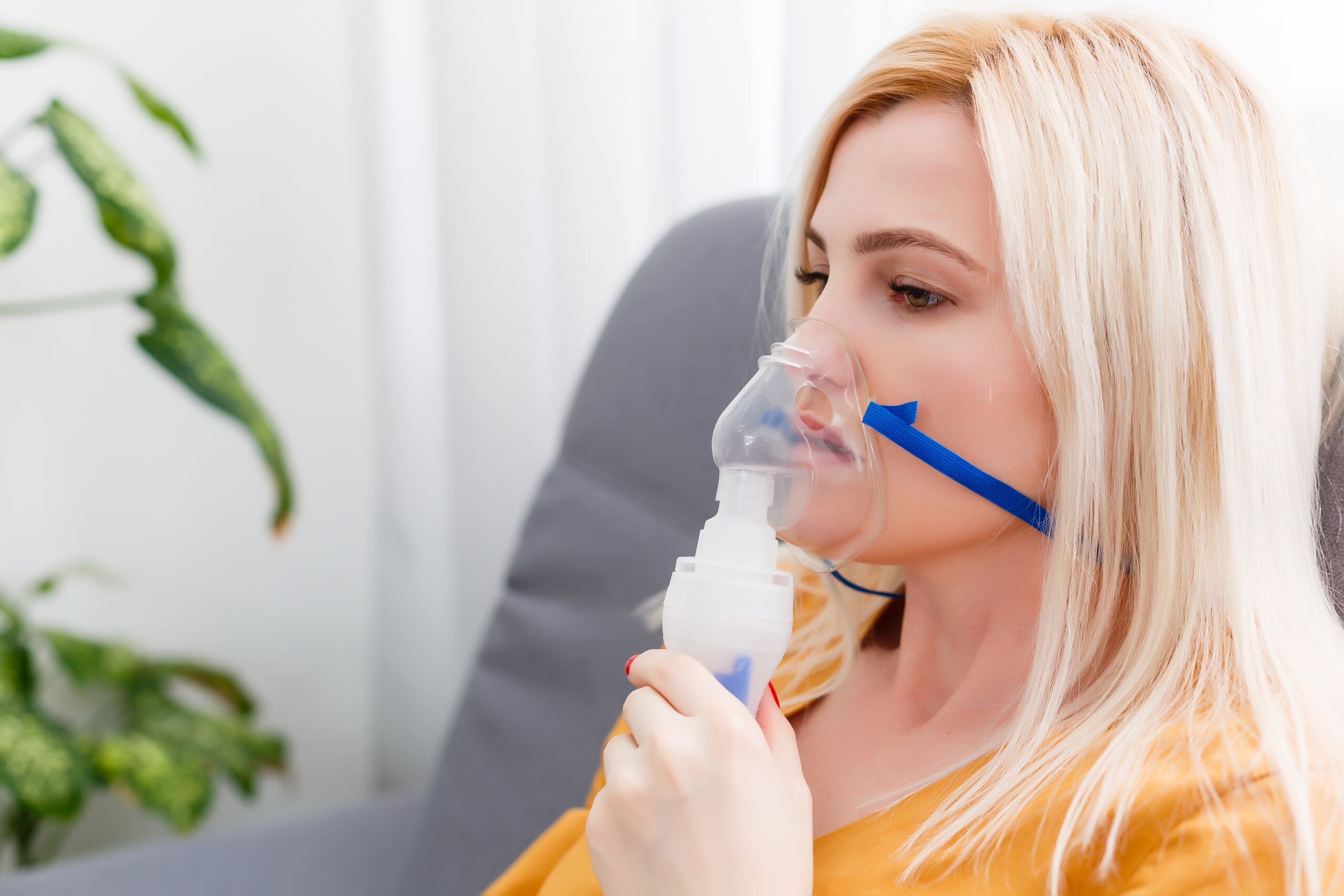 A woman uses a nebulizer with an oxygen mask at home to manage her breathing difficulty