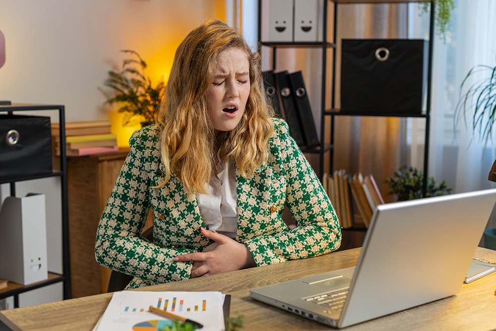 Woman at her desk suddenly grabbing her abdominal area in pain