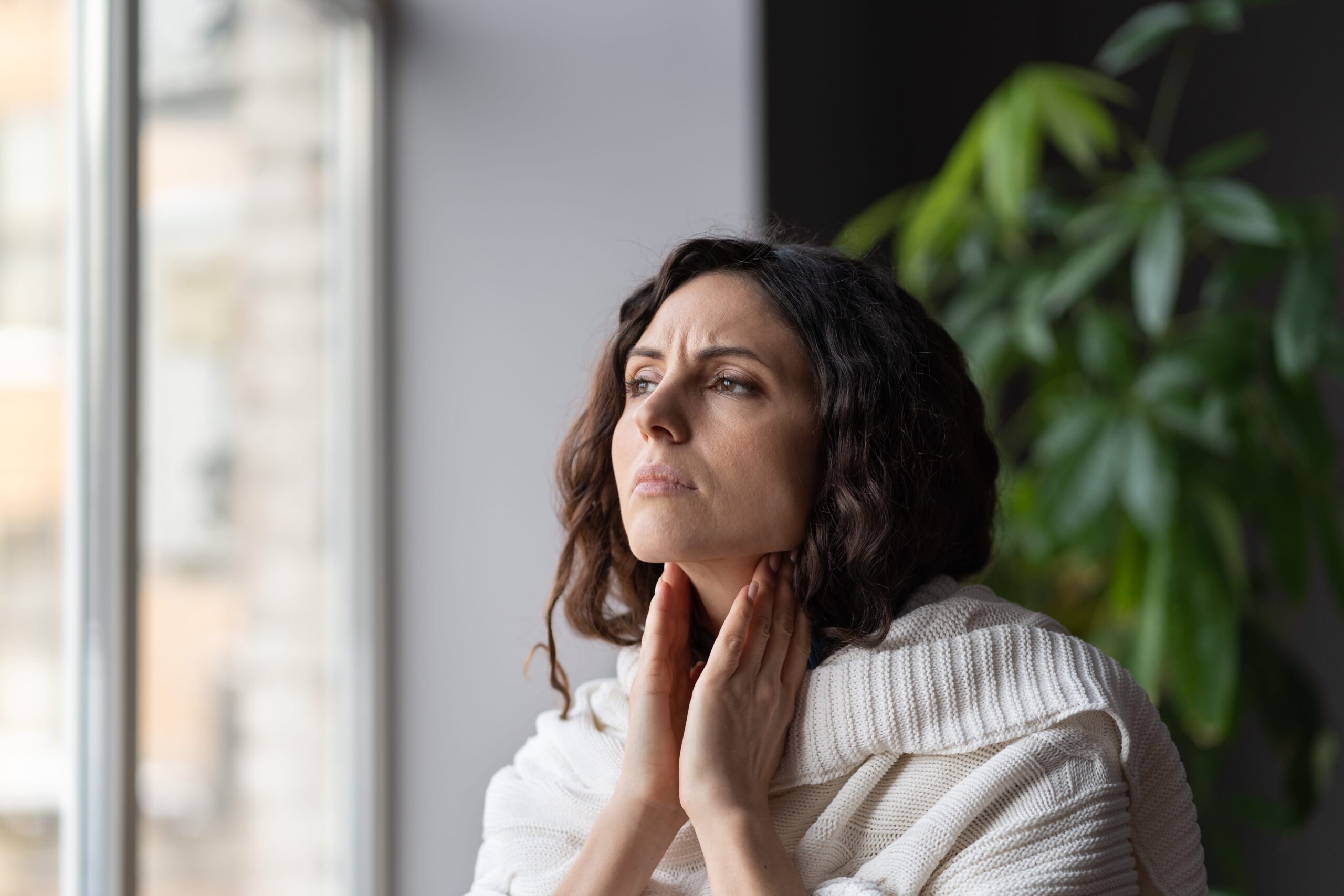Woman touching her neck with pained expression, indicating discomfort.