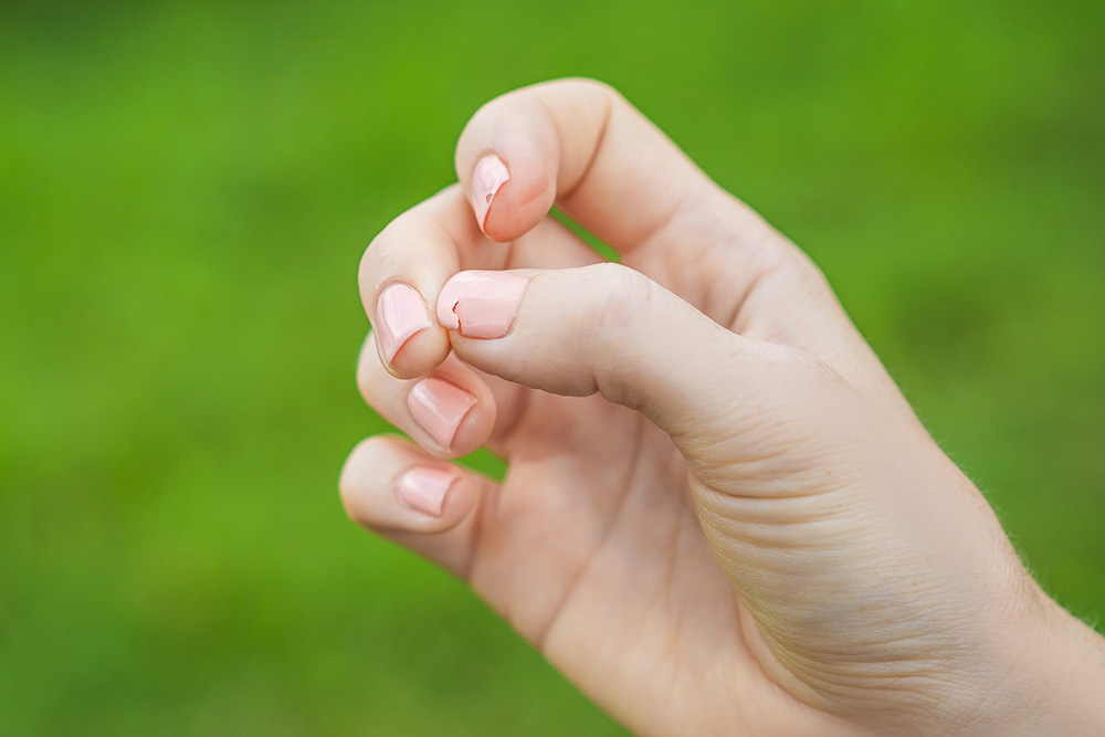 Woman's hand with pink manicured nails showing one broken nail against a green background.